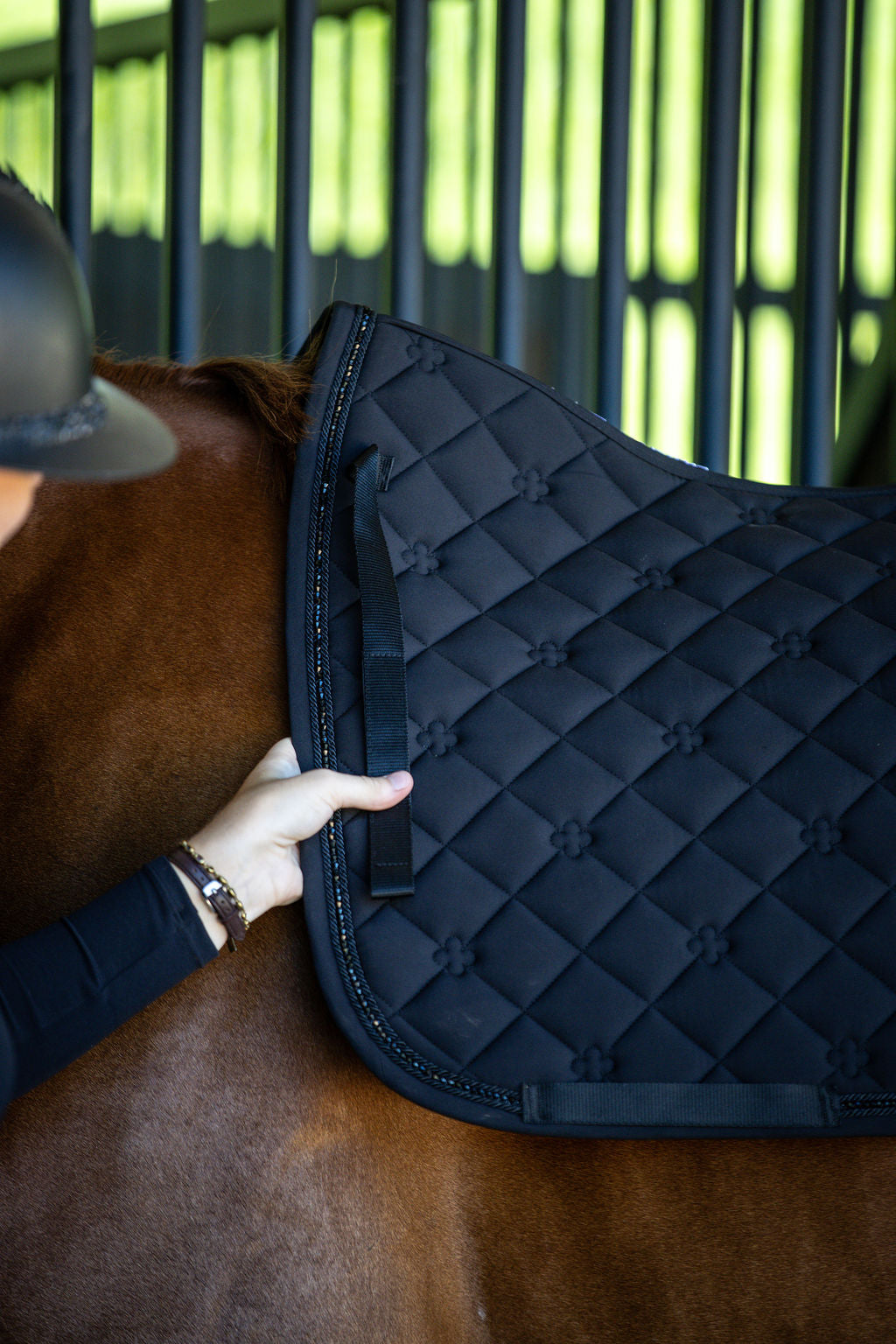 Person adjusting a black quilted saddle pad on a horse 