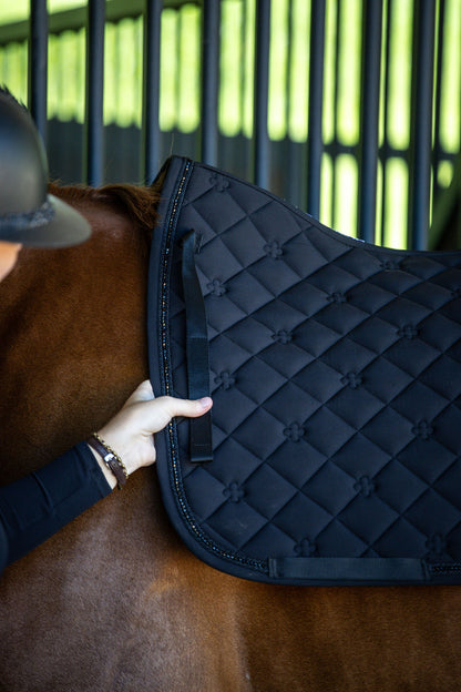 Person adjusting a black quilted saddle pad on a horse 