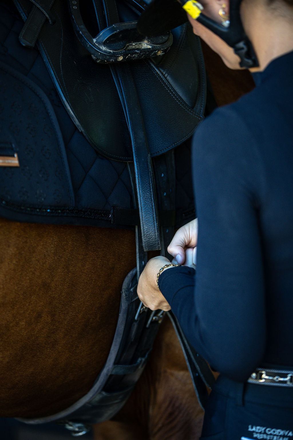 Person adjusting a black saddle on a horse