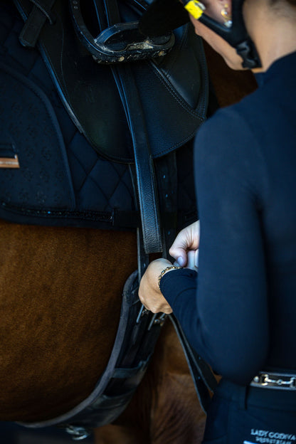 Person adjusting a black saddle on a horse